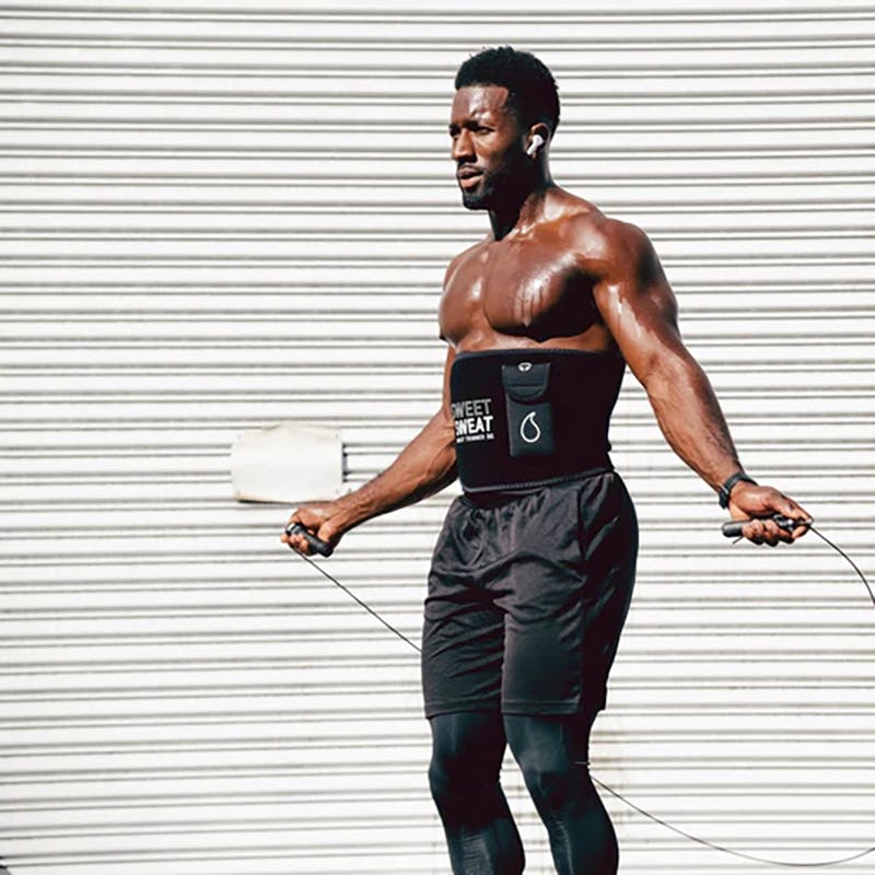 A man jumping rope while wearing a Sweet Sweat® Xtra Coverage waist trimmer with a Sweet Sweat® phone holder attached to it.
