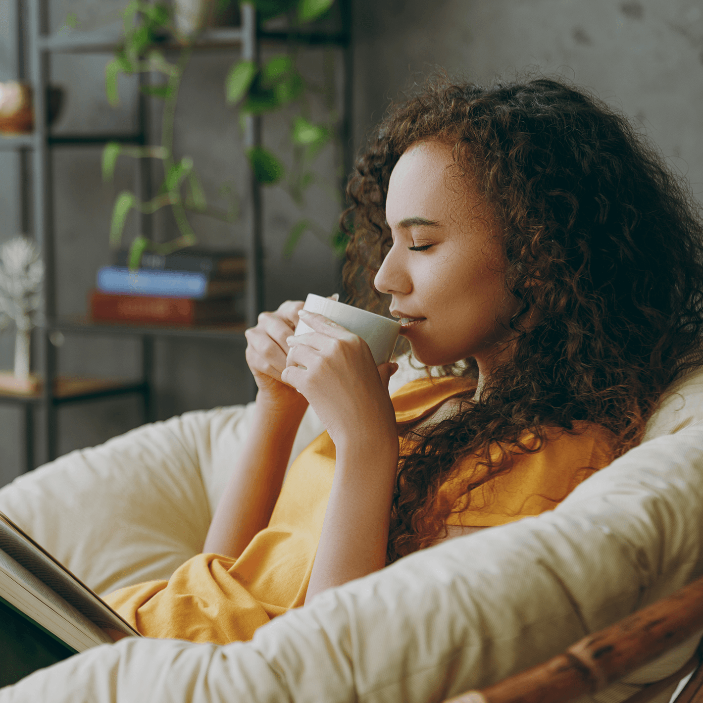 Woman sitting in a circular wicker lounge chair sipping coffee from a ceramic mug.