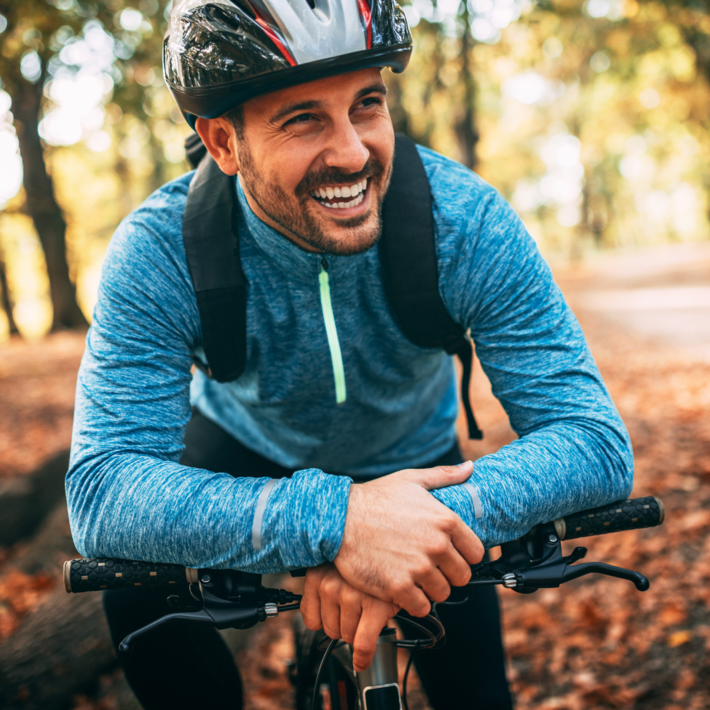 Man smiling, while resting his arms on his mountain bike out in nature.
