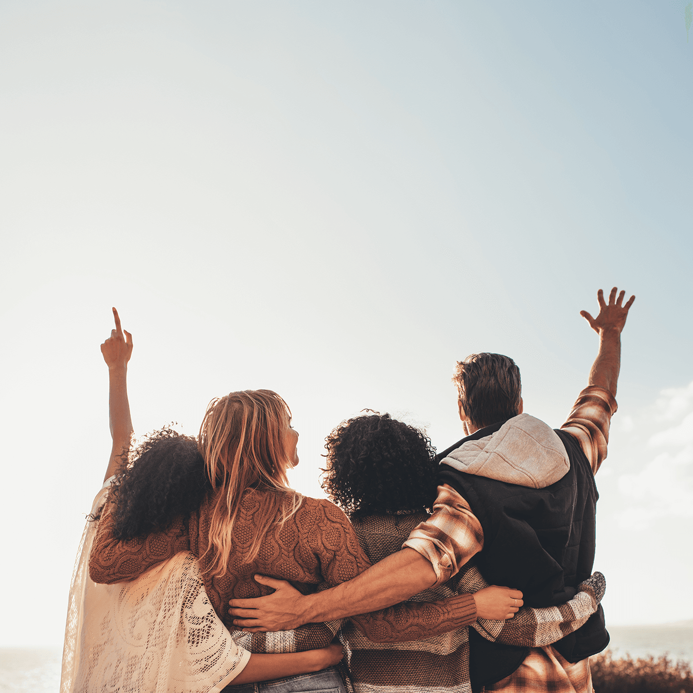 A group of friends with their hands around each others waists looking towards the horizon with their backs to the camera.