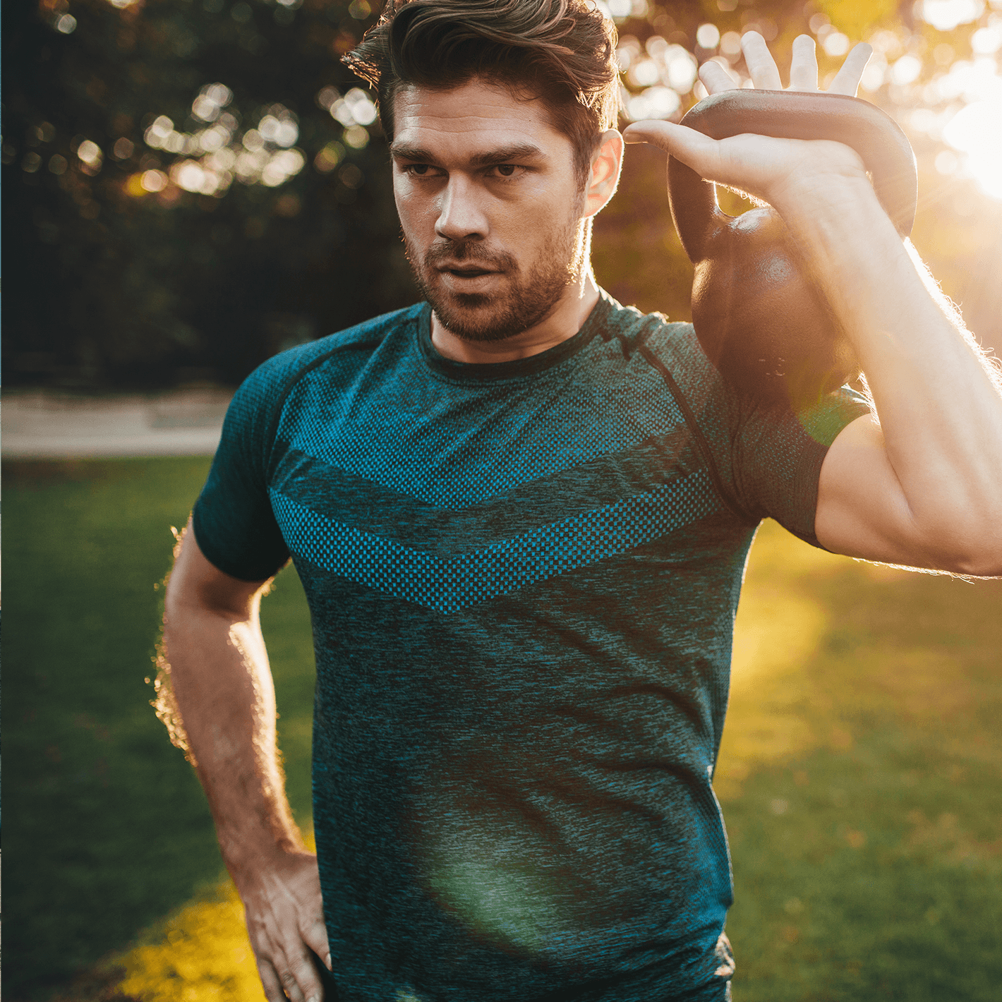 Man working out outdoors with a weighted kettlebell resting on his shoulder.