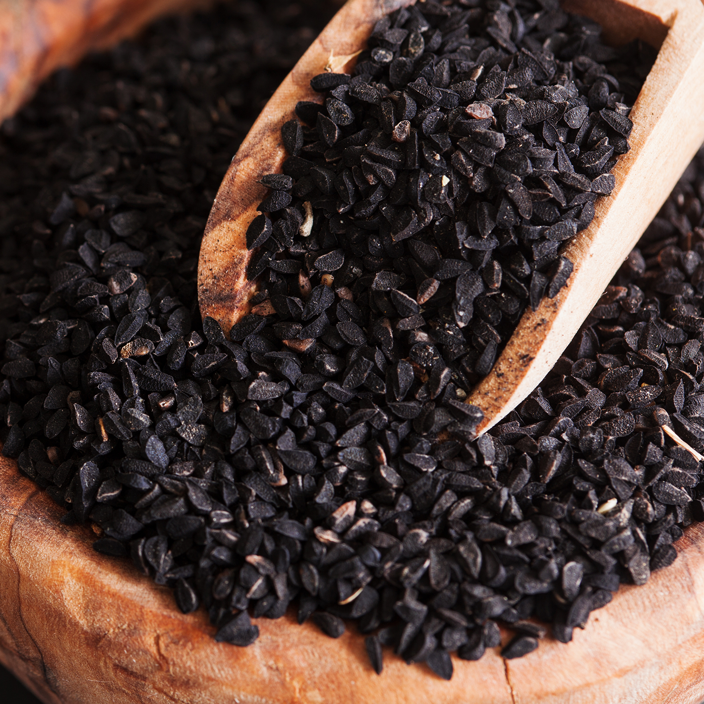 Black Cumin seeds in a bowl with a set of tongs to pick them up.