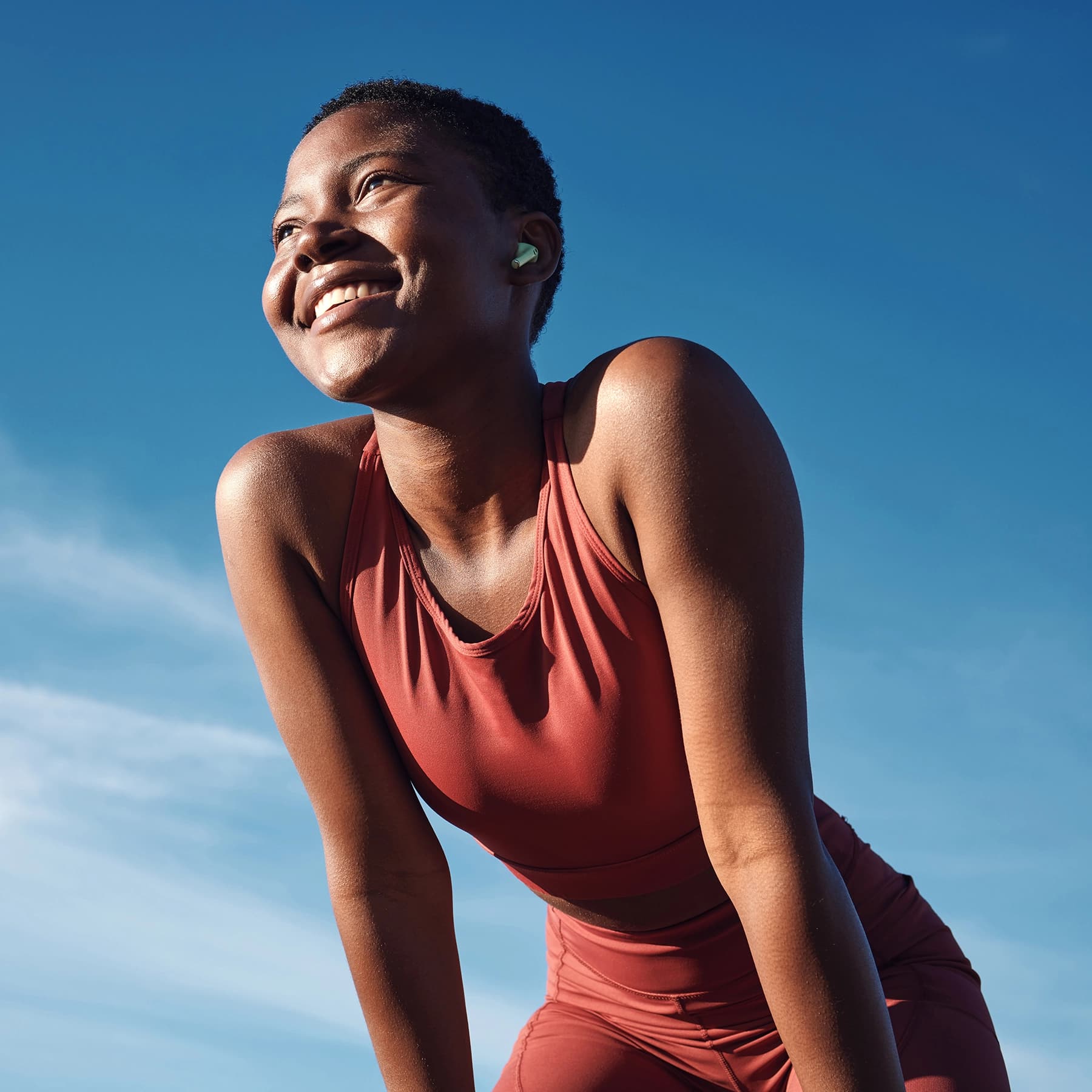 Woman smiling, in workout attire outdoors with her hands on her knees.