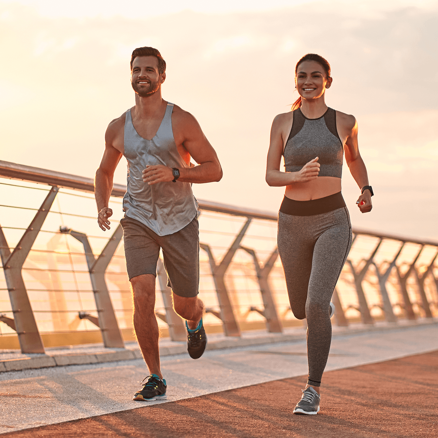 A man and woman jogging together outside on a bridge.