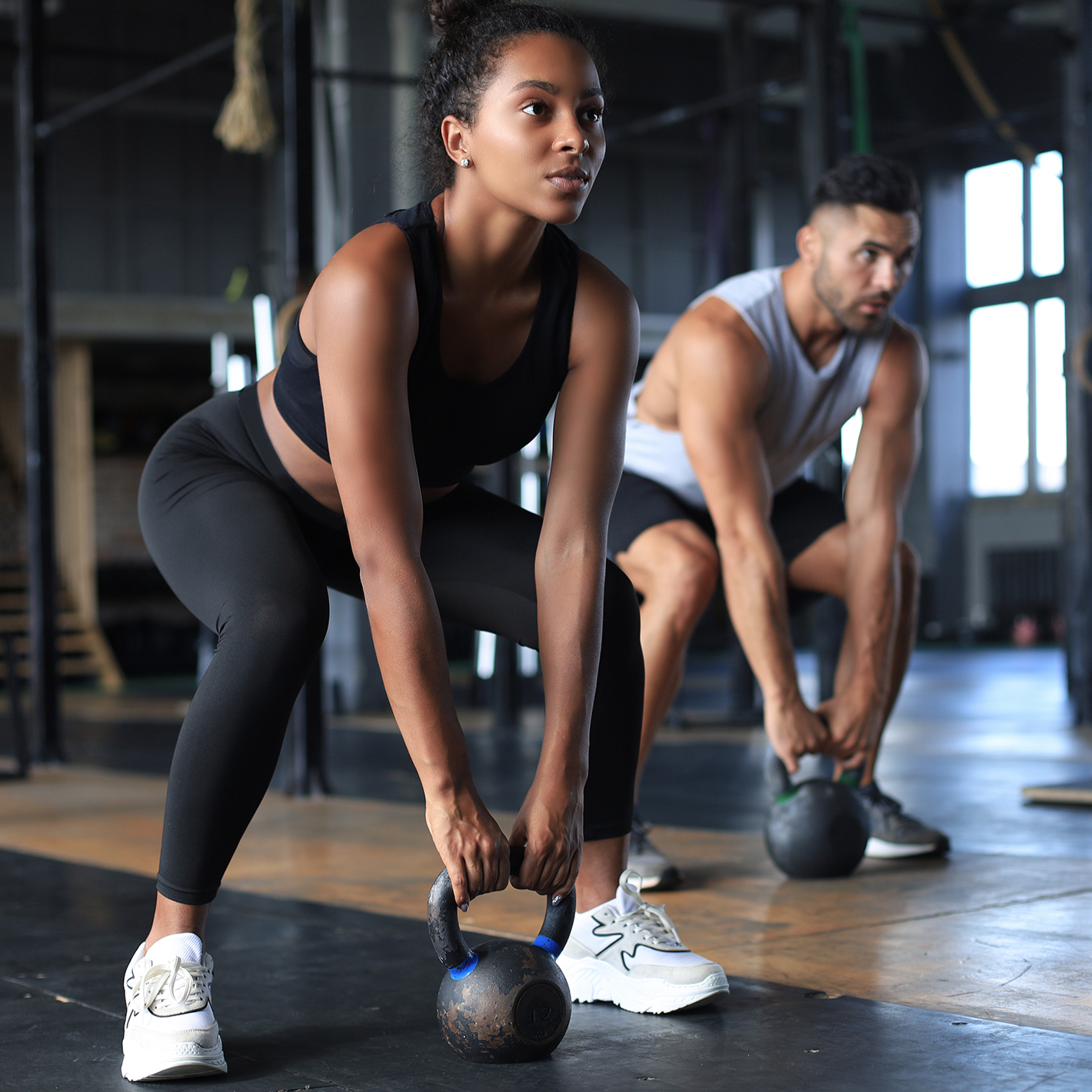 A man and a woman working out with weighted kettle bells.