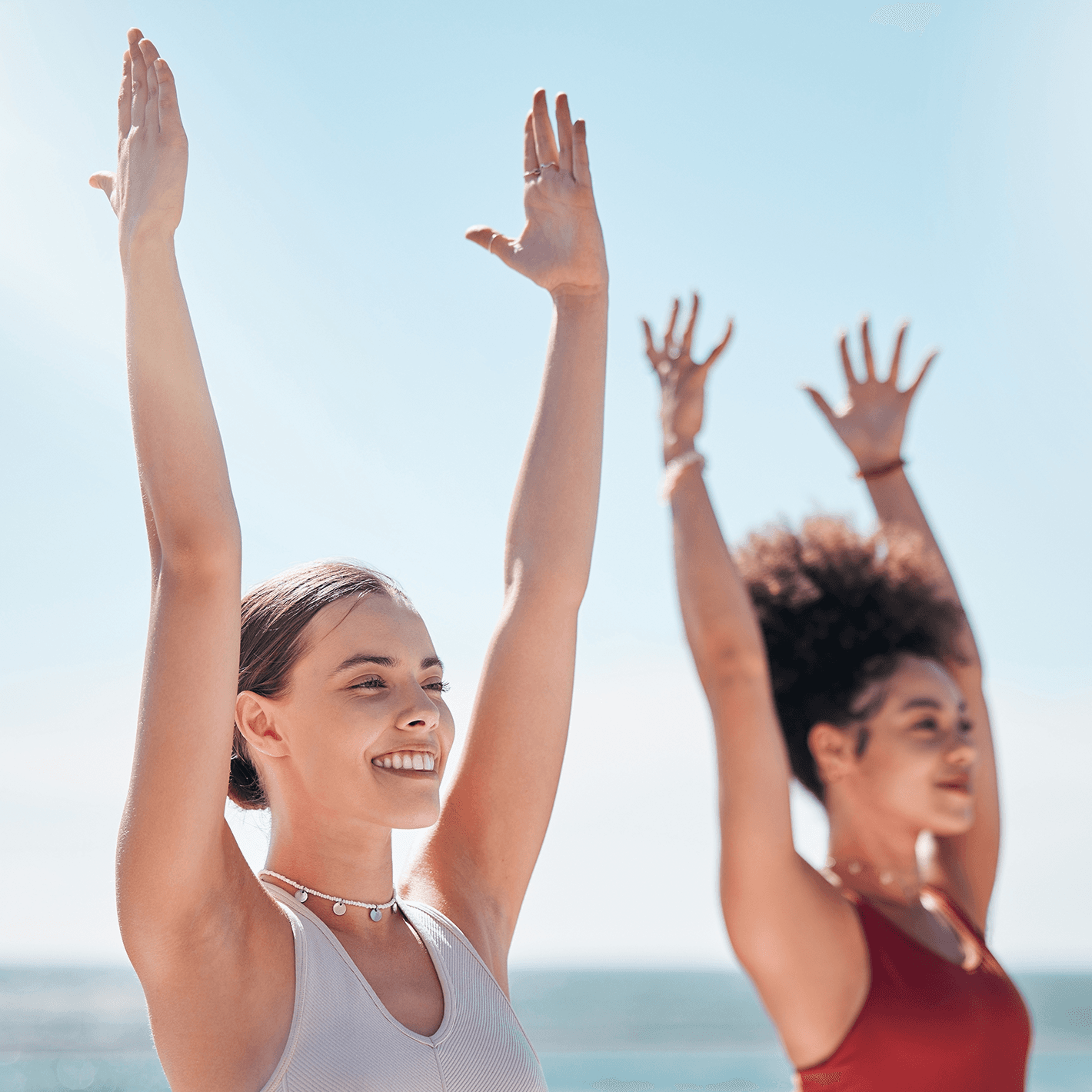 Two women with arms stretched upward in the outdoors.