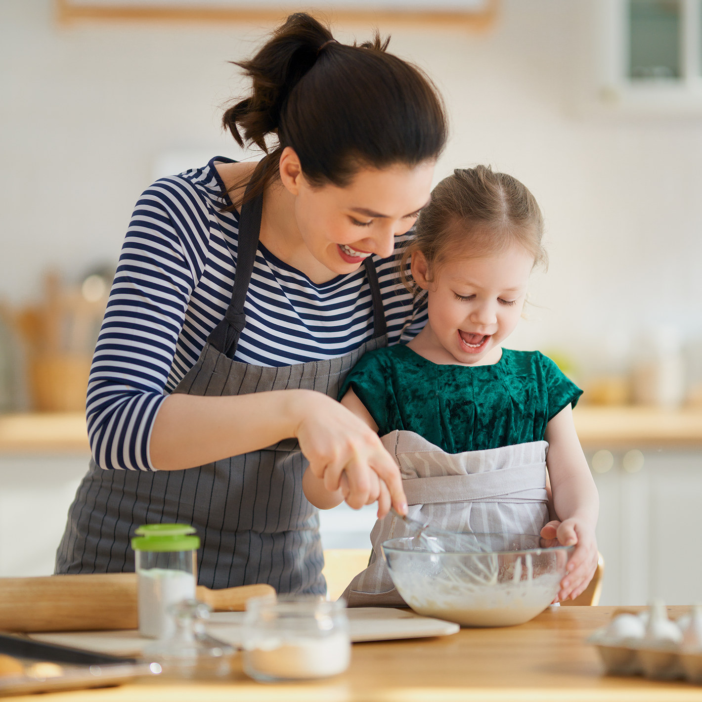 Woman and her daughter mixing something in a bowl in a kitchen while both are smiling.