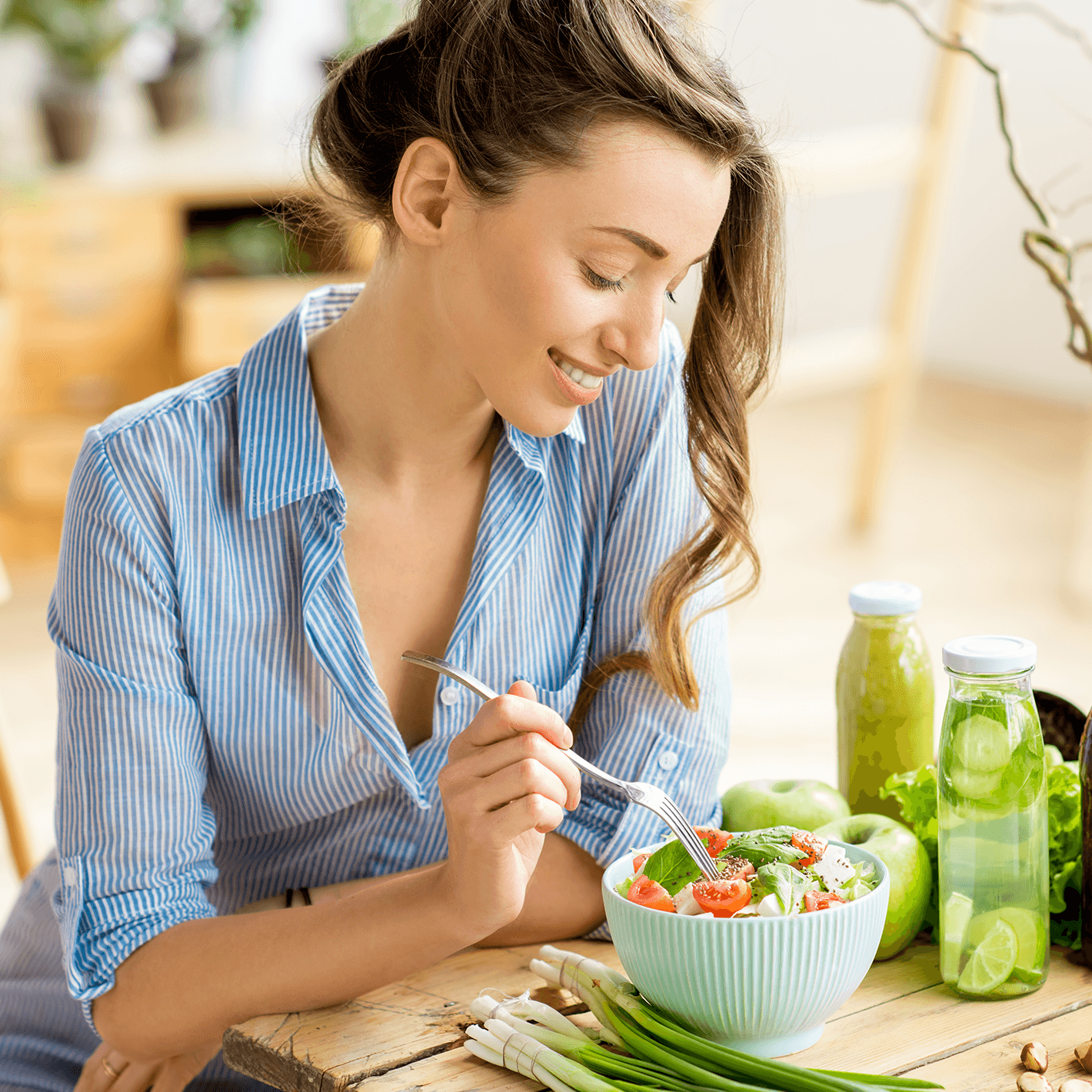 Woman sitting at a table eating a salad, with assorted vegetables surrounding the bowl.