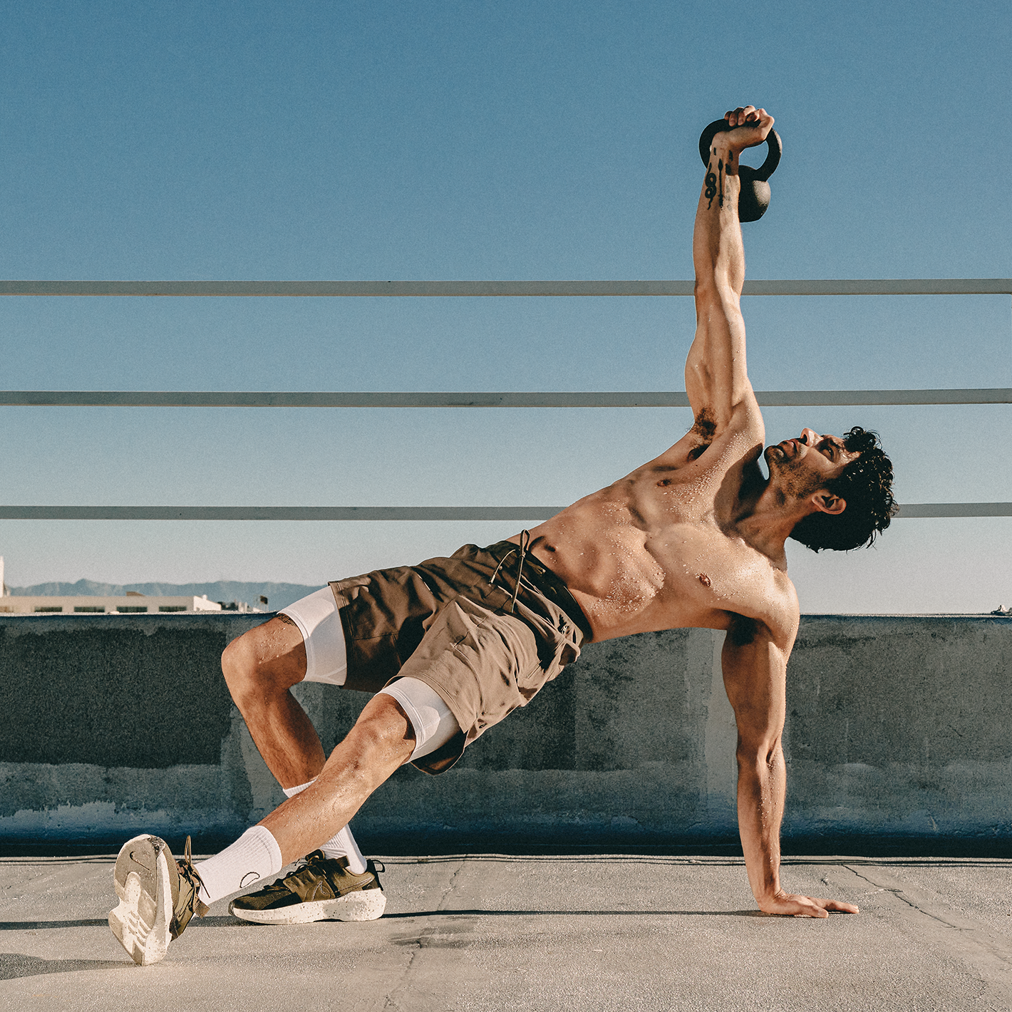 Man outdoors lifting a weighted kettlebell over his head, while stretching.