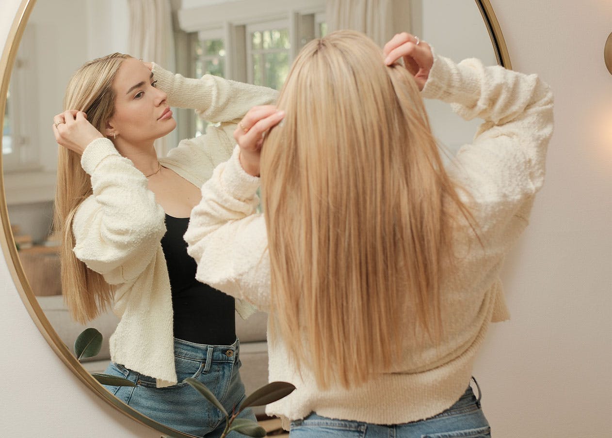 Woman looking in mirror while fixing her hair.