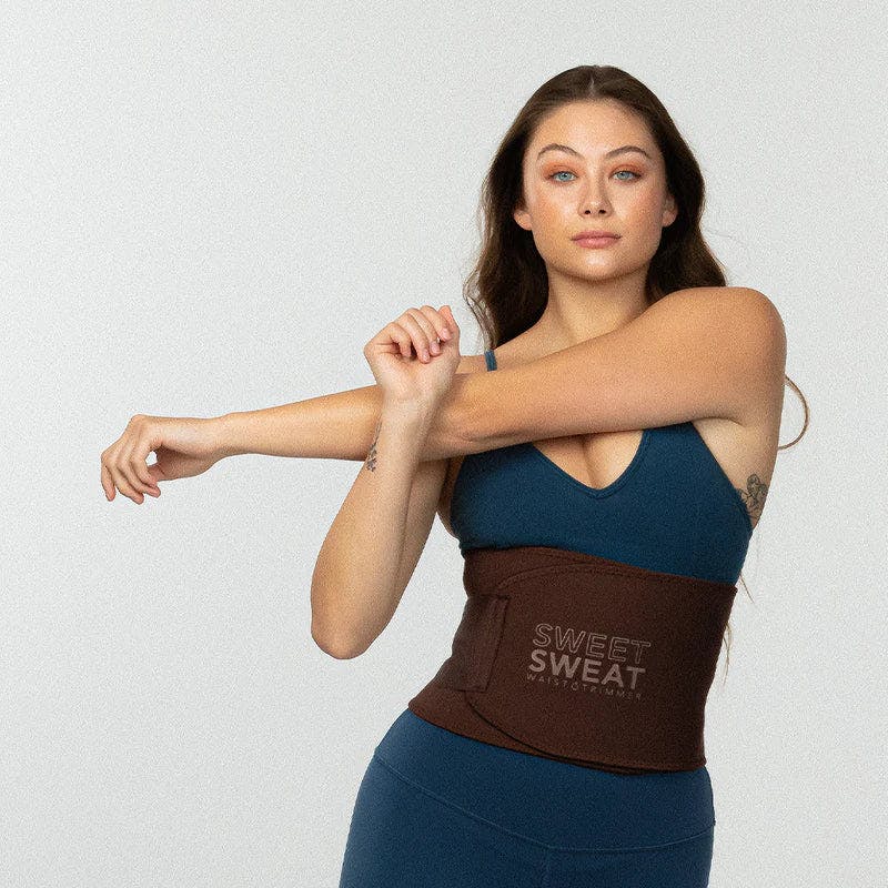 Woman stretching while wearing a Sweet Sweat® Toned waist trimmer around her waist.