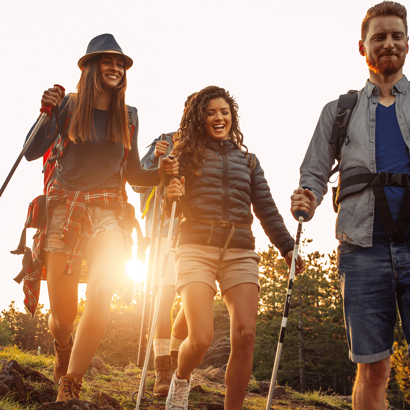 A group of people using hiking poles to hike down a hill on a sunny day.