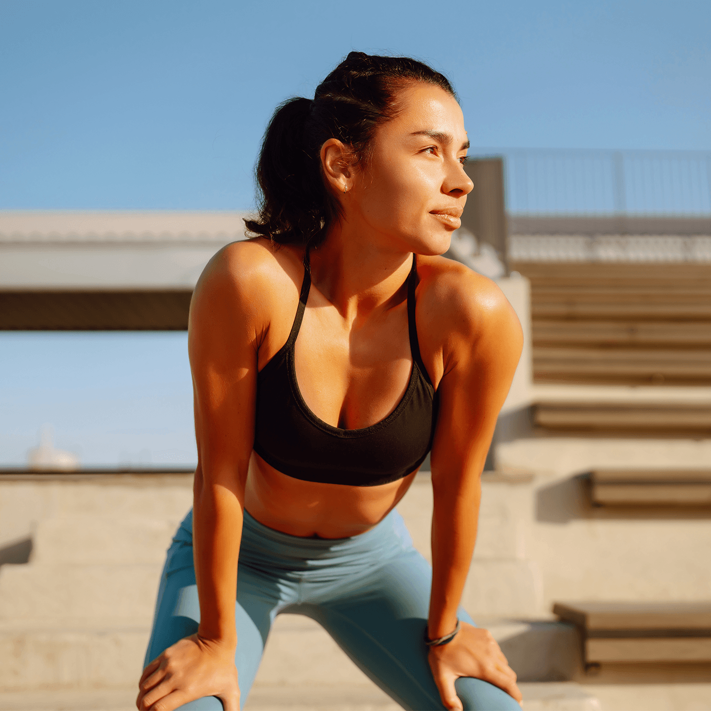 A woman in workout gear bending over, hands on knees, outside.