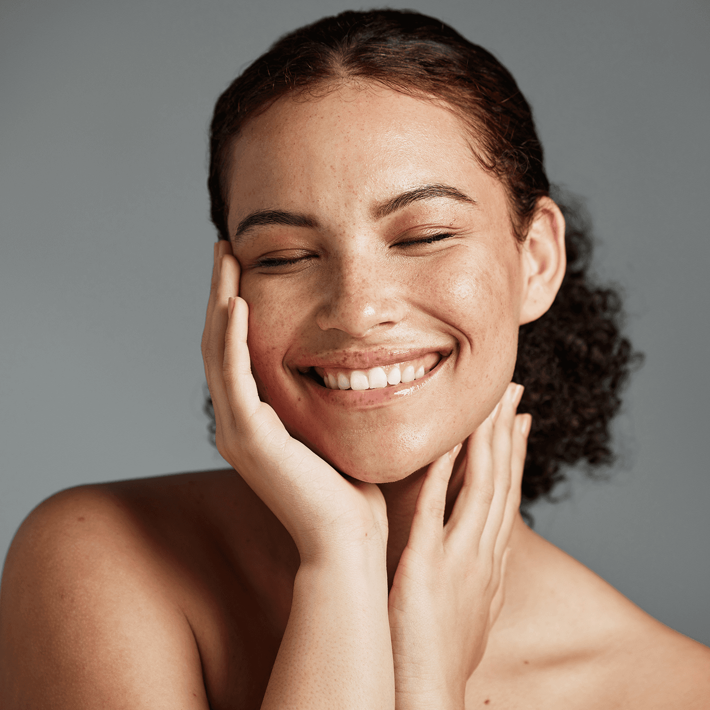 A woman smiling at the camera with her hands on her cheeks.